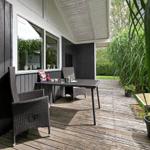 Terrasse mit Tisch, Stühlen und Pflanzen neben Hauswand.