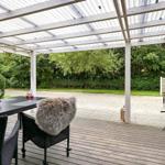 Terrasse mit Tisch, Stühlen und Grill unter Dach.