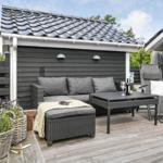 Terrasse mit Sitzgruppe, Tisch und Pflanzen vor schwarzem Holzhaus