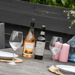 Außenbereich mit Tisch, zwei Flaschen, Gläsern, Kerzen und Blumen in einem Blumentopf.