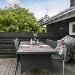 Terrasse mit Tisch, Stühlen, Grill und Blick auf grüne Hecke.