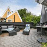 Terrasse mit Sitzgelegenheiten, Tisch und Grill. Im Hintergrund gelbes Haus.