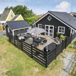 Schwarzes Ferienhaus mit Terrasse, Sitzgruppe und Sonnenschutz. Grün umgeben.