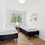 Zwei Einzelbetten, Fenster mit Blick auf Bäume, Wandbilder und Holzboden.