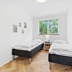 Zwei Betten mit weißer Bettwäsche, Holzboden und Fenster mit Blick auf Bäume.