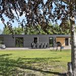 Moderne Villa mit Terrasse, Garten und Grillplatz unter Bäumen.