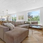 Wohnzimmer mit Ecksofa, Glas-Tisch und Holzboden. Küche im Hintergrund mit Esstisch.