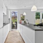 Moderne Küche mit weißen Schränken und dunklem Arbeitsplatz. Durchgang zur Terrasse mit Gartenblick.