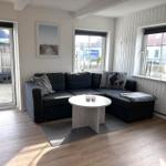 Ein Wohnzimmer mit einem schwarzen Sofa, einem runden Tisch und Fenstern mit Blick nach draußen.