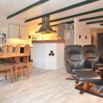 Küche mit Essbereich und Wohnzimmer mit Ledersesseln und Holzmöbeln.