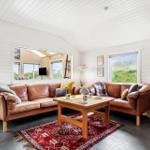 Wohnzimmer mit braunem Ledersofa, Holztisch und rotem Teppich.