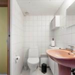 Badezimmer mit Toilette, Waschbecken und Spiegel. Weiße Fliesen und Holzdecke.