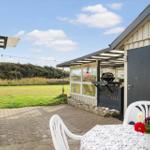 Terrasse mit Tisch, Stühlen und Blumen. Hintergrund: Grasland und Bäume.