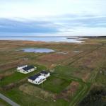 Zwei Häuser auf einer grünen Wiese am Wasser mit Blick auf die Landschaft.