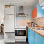 Küche mit blauen Schränken, Kühlschrank und Herd. Fenster mit Blick auf Grün.