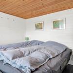 Schlafzimmer mit Doppelbett, weißen Wänden und Holzdecke. Zwei Nachttische mit Lampen.