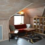 Ein Wohnzimmer mit Holzwand, rotem Sofa, Bücherregal und Holztisch.