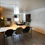 Essbereich mit Tisch und Stühlen, Wohnbereich mit Sofa und Fernseher, Holzboden und weiße Wände.