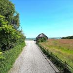 Hütte am Wasser mit Grünstreifen und Zaun entlang eines Kieswegs.