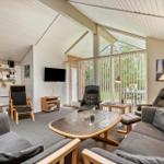 Wohnzimmer mit Sofa, Sessel und TV. Große Glasfront mit Blick auf Garten.