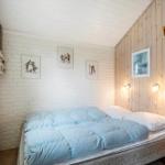 Schlafzimmer mit Bett, Holzwand und weißen Ziegelwand. Bilder an der Wand. Nachttische mit Lampen.