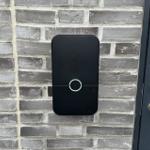 Schwarze Türöffneranlage an grauer Ziegelwand neben dunkler Tür