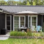 Haus mit Terrasse, Garten und Sitzgelegenheiten unter Sonnenschirm.