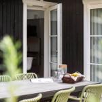 Außenbereich mit Tisch und Stühlen vor einem Haus mit offenen Türen.