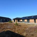 Zwei moderne Häuser mit dunklem Dach und großen Fenstern stehen auf einer grasbewachsenen Fläche.