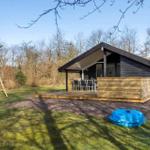 Moderne Holzhütte mit Terrasse, Spielplatz und blauem Pool im Grünen.