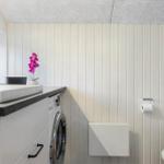 Badezimmer mit Waschmaschine, Spülbecken und Toilette. Wandverkleidung und Decke sichtbar.