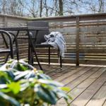 Terrasse mit Tisch, Stühlen und Decken. Holzgeländer und Bäume im Hintergrund.