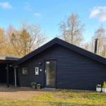 Schwarzes Holzhaus mit Carport und Garten. Hintergrund: Bäume und klarer Himmel.