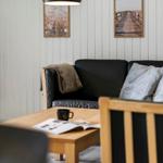 Ein Wohnzimmer mit schwarzer Ledercouch, Holztisch und Wandbildern.