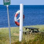 Schild mit C 675 und Rettungsring an Strand. Picknicktisch im Hintergrund.