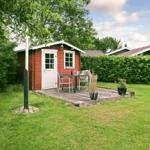 Rotes Holzhaus mit Terrasse, Tisch, Stühlen und Pflanzen im Garten.