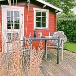 Roter Holzschuppen mit Terrasse, Tisch und Stühlen im Garten.