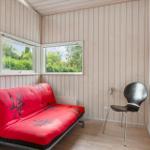 Raum mit rotem Futon, schwarzer Stuhl und Holzwand. Zwei Fenster zeigen grüne Bäume.