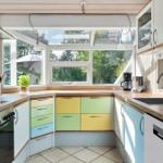 Küche mit farbigen Schubladen, Holzoberflächen und großem Fenster zur Außensicht.