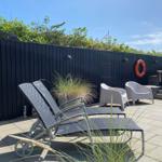 Terrasse mit Liegestühlen, Sitzgelegenheiten und Pflanzen vor dunkler Holzwand.