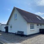 Weißes Haus mit schwarzem Dach und Fenstern. Vorgarten mit Bank und Pflanze.