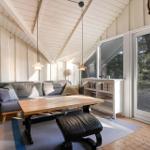 Wohnraum mit Sofa, Tisch und Bücherregal. Holzdecke und große Fenster.