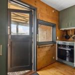 Küche mit grünen Schränken und Holzwand. Tür führt nach draußen.