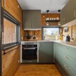 Küche mit Holzwänden, grünen Schränken und Fenster zum Garten.