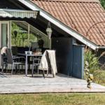 Terrasse mit Tisch und Stühlen unter einem Vordach. Im Hintergrund ist das Haus mit Fenstern zu sehen.