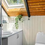 Badezimmer mit Dusche, Waschbecken und Toilette unter Holzdecke mit Dachfenster.