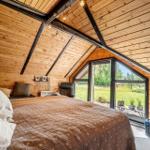 Schlafzimmer mit Holzwand und großem Fenster. Bett, Sessel und Bücherregal sind sichtbar.