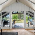 Haus mit Holzboden und großem Glasbereich zur Terrasse. Draußen Tisch, Stühle und Garten.