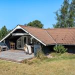 Ein Ferienhaus mit Holzterrasse und braunem Dach unter blauem Himmel.