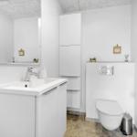 Badezimmer mit Waschbecken, Spiegel, Toilette und Schränken.